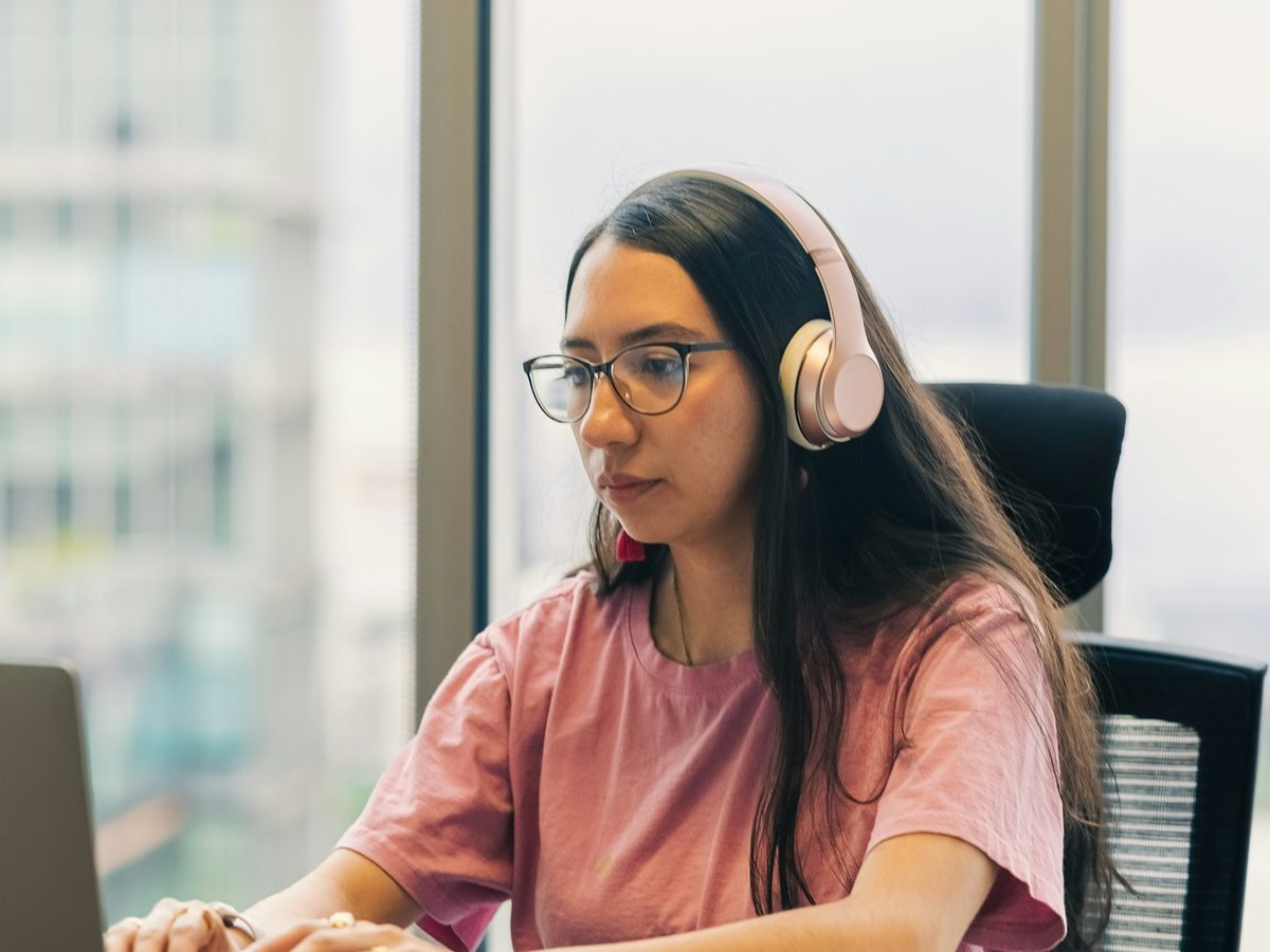 A virtual assistant working at a laptop, headphones on, notebook open beside her